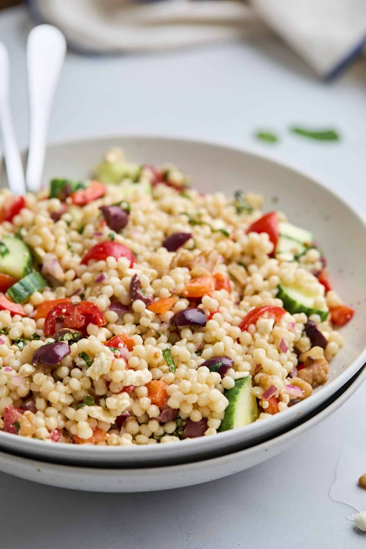 A vibrant Mediterranean couscous salad featuring Israeli couscous, cucumbers, tomatoes, olives, and feta, served in a bowl.