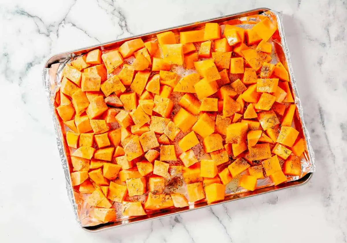 Diced butternut squash and sweet potatoes seasoned and spread on a baking sheet.