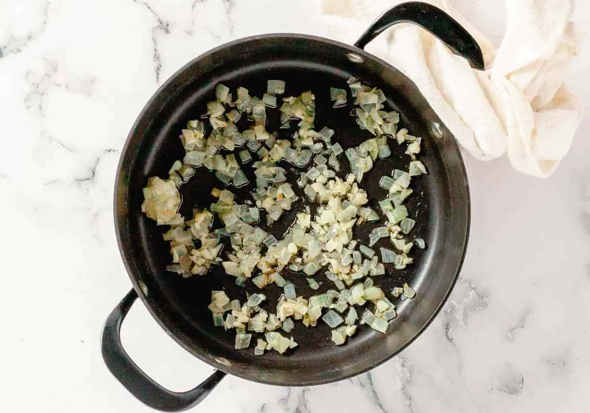 Sautéed onions and garlic in a black pot, the base for a flavorful butternut squash and sweet potato soup.