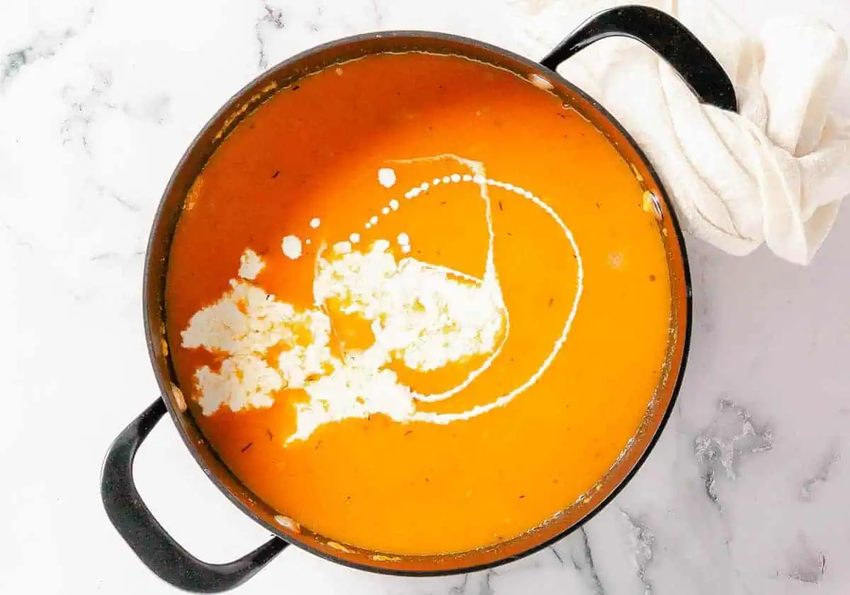 Butternut squash and sweet potato soup in a pot, with a swirl of cream added for richness.