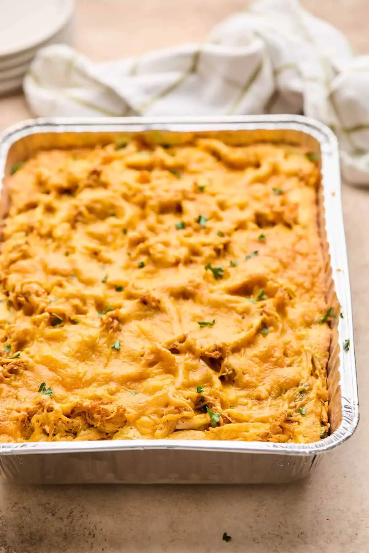 Baked chicken cornbread casserole in a foil pan, topped with a golden layer of melted cheese and garnished with fresh parsley.