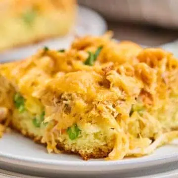 A close-up of a piece of chicken cornbread casserole on a white plate, focusing on the fluffy cornbread base, tender chicken, and melted cheese.