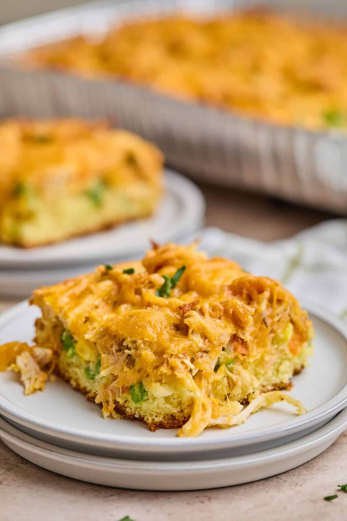 A square piece of chicken cornbread casserole on a white plate, highlighting the cheesy, golden top and the moist cornbread base with vibrant vegetables.