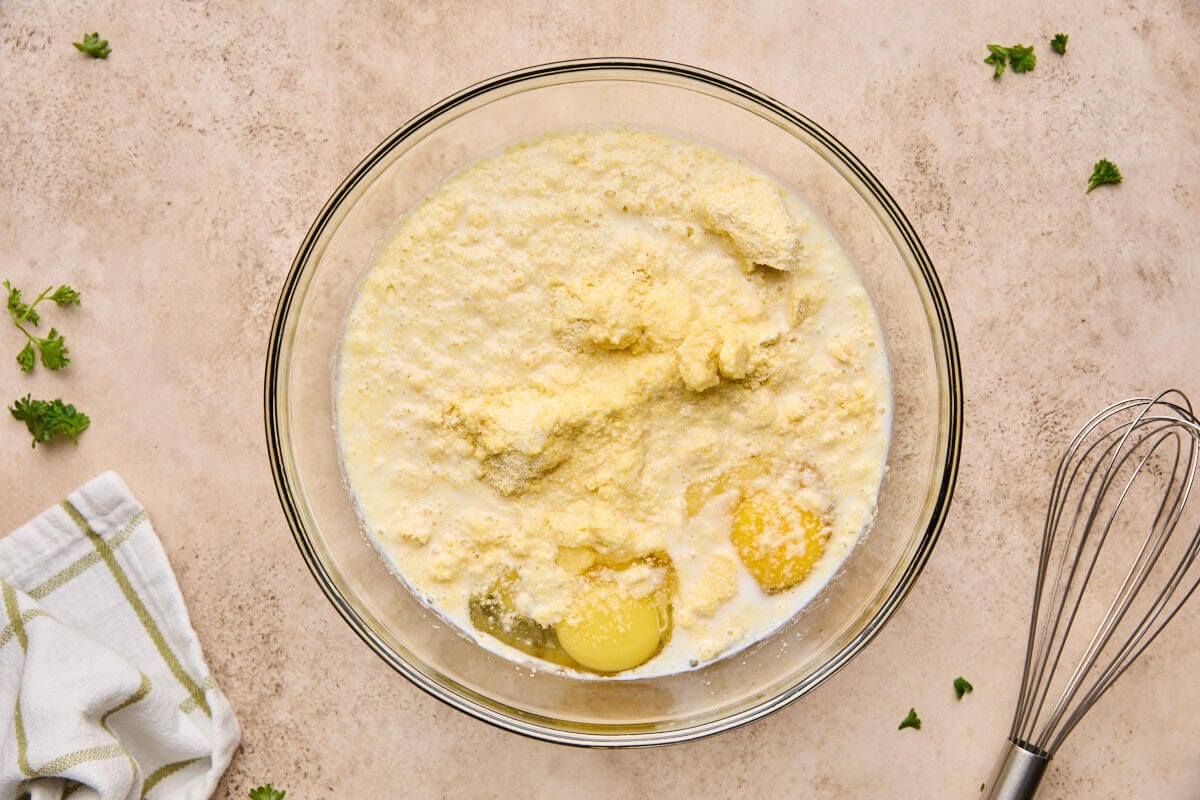 A large glass bowl filled with corn muffin mix, eggs, milk, and chicken broth, ready to be whisked for the chicken cornbread casserole.