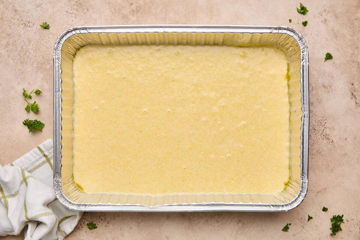 Cornbread batter evenly spread in a greased baking dish.