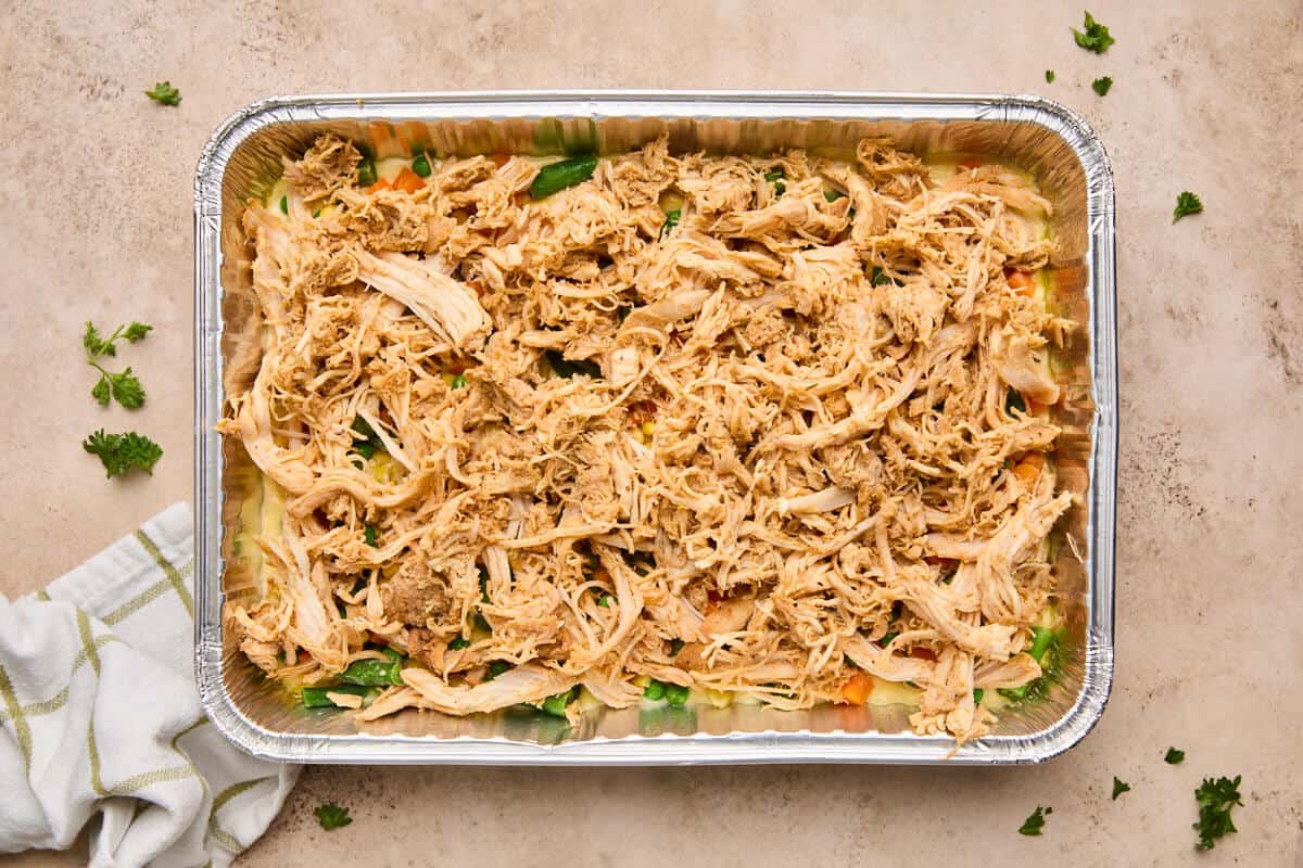 Shredded chicken layered on top of the mixed vegetables in the baking dish.