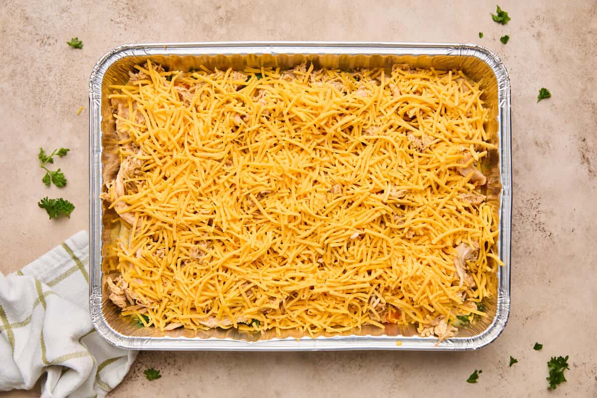 The chicken cornbread casserole topped with a generous layer of shredded cheddar cheese, just before baking.