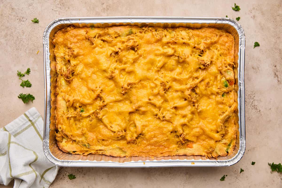 Baked chicken cornbread casserole in a foil baking dish, golden brown with melted cheddar cheese on top