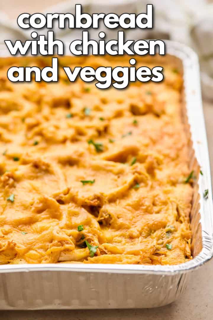 A close-up of the baked chicken cornbread casserole in a foil pan with text overlay reading "cornbread with chicken and veggies" in bold black letters.