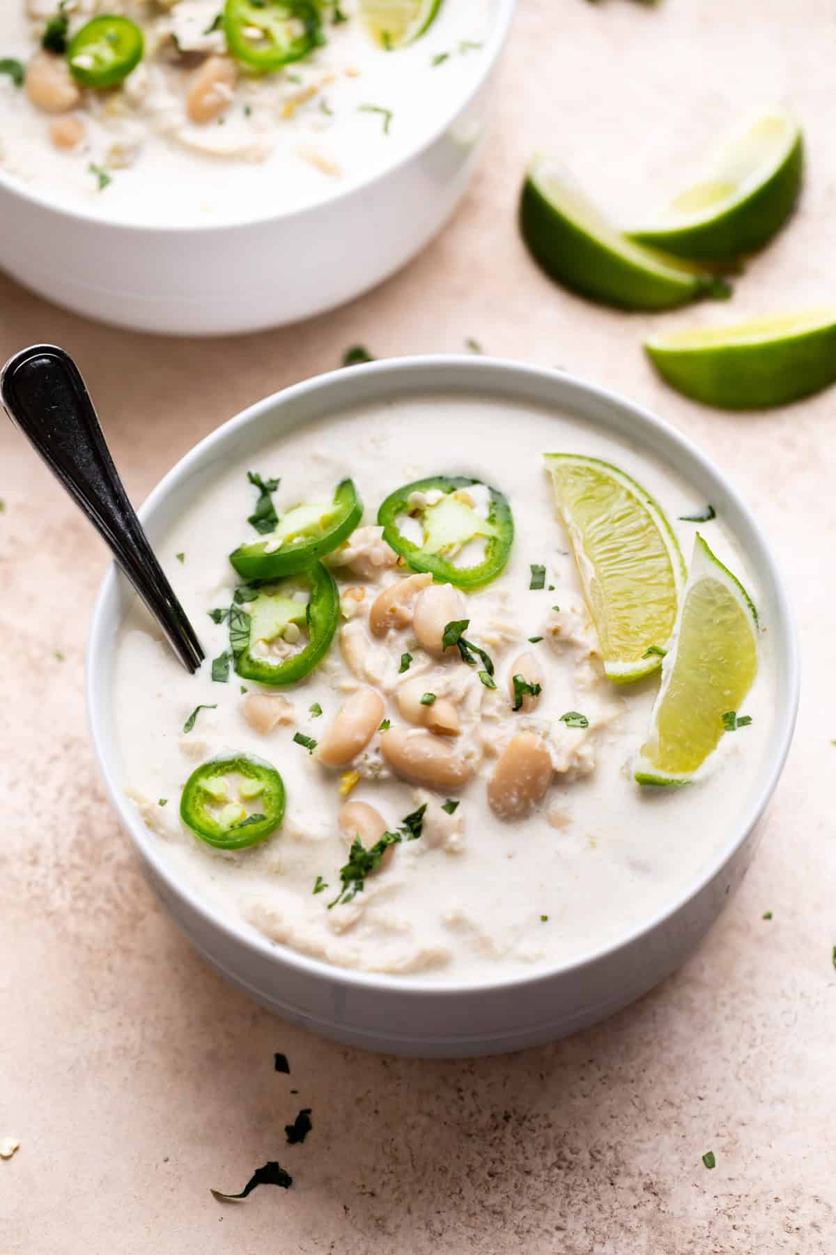 Creamy slow cooker white chicken chili served in bowls, garnished with sliced jalapeños and lime.