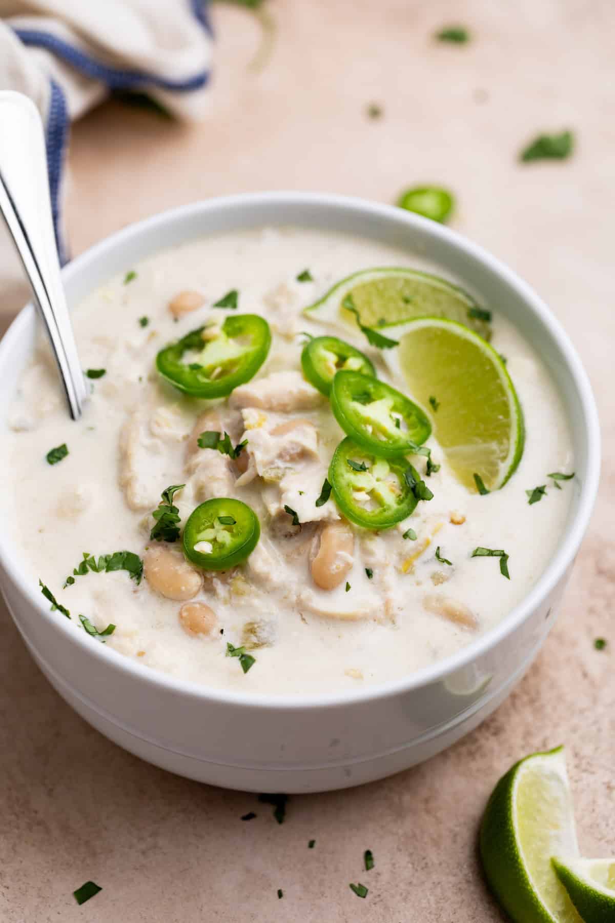 Creamy white chicken chili slow cooker recipe in a bowl, topped with jalapeños and lime, a healthy and cheap crock pot meal option.