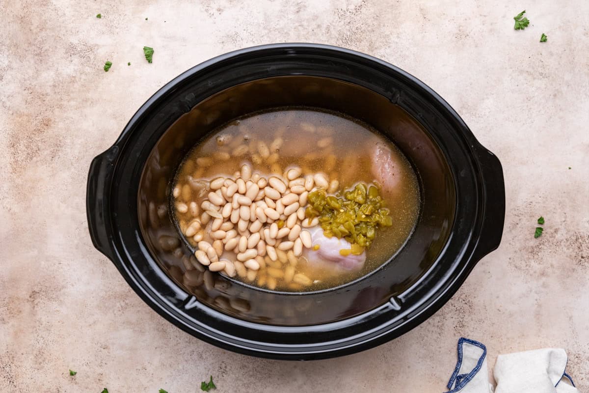 Uncooked crock pot white chicken chili ingredients, including chicken breasts, white beans, and green chiles, placed in a slow cooker before cooking.