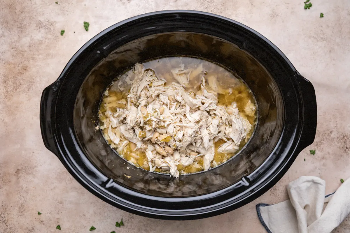 Cooked chicken and white beans in broth inside a slow cooker.