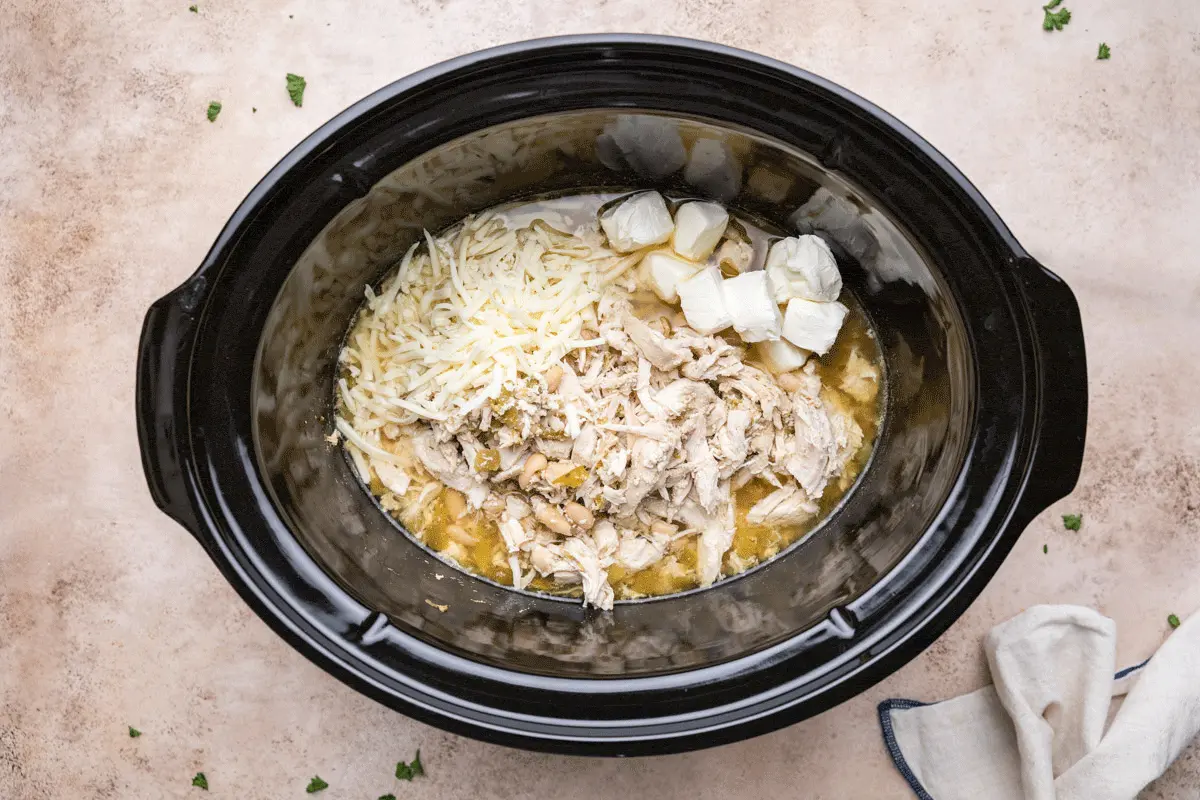 Cooked crock pot white chicken chili with added shredded cheese and cubed cream cheese.