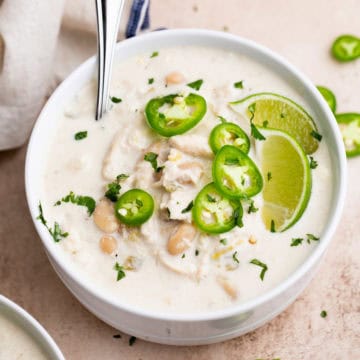 Creamy slow cooker white chicken chili topped with sliced jalapeños and lime wedges.