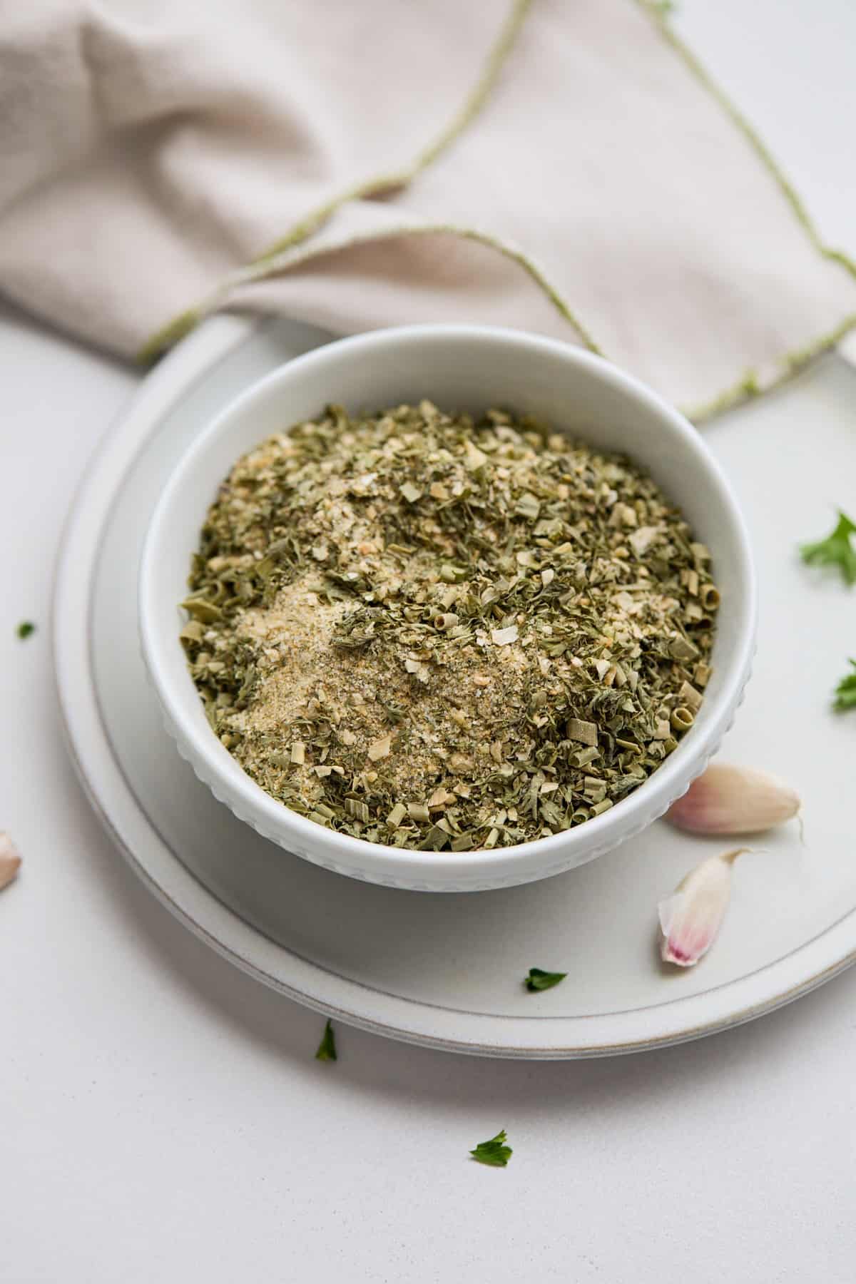 Homemade ranch dressing mix in a white bowl, with a napkin and garlic cloves nearby.