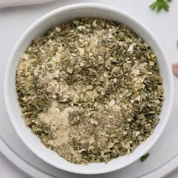 A close-up view of a bowl filled with homemade ranch dressing mix, featuring a blend of dried herbs and spices.