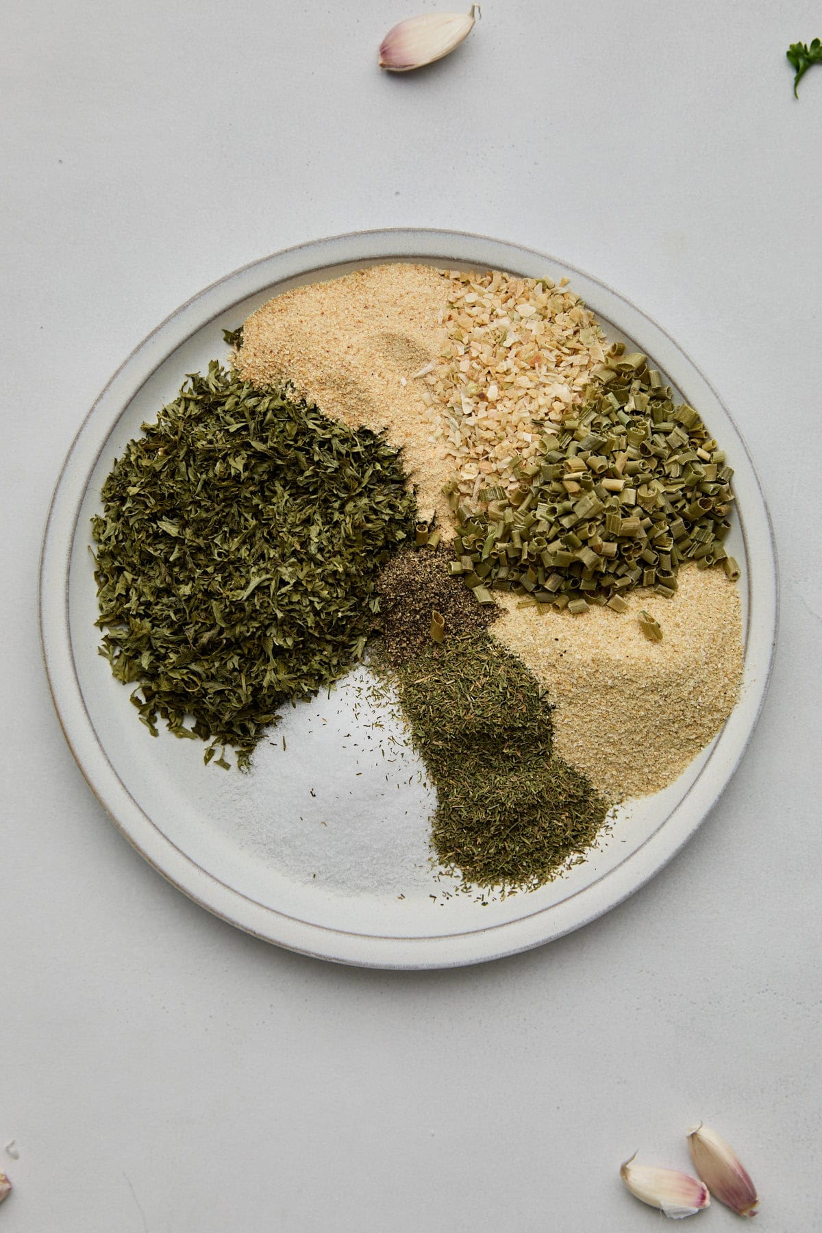 A variety of dried herbs and spices displayed on a plate, showcasing the ingredients for ranch dressing mix.