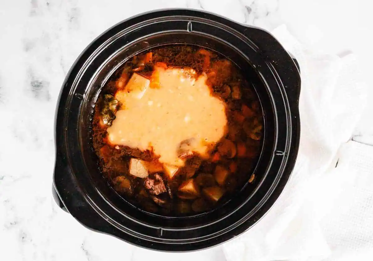 Thickened beef stew in the slow cooker, with visible chunks of potatoes, beef, and carrots.