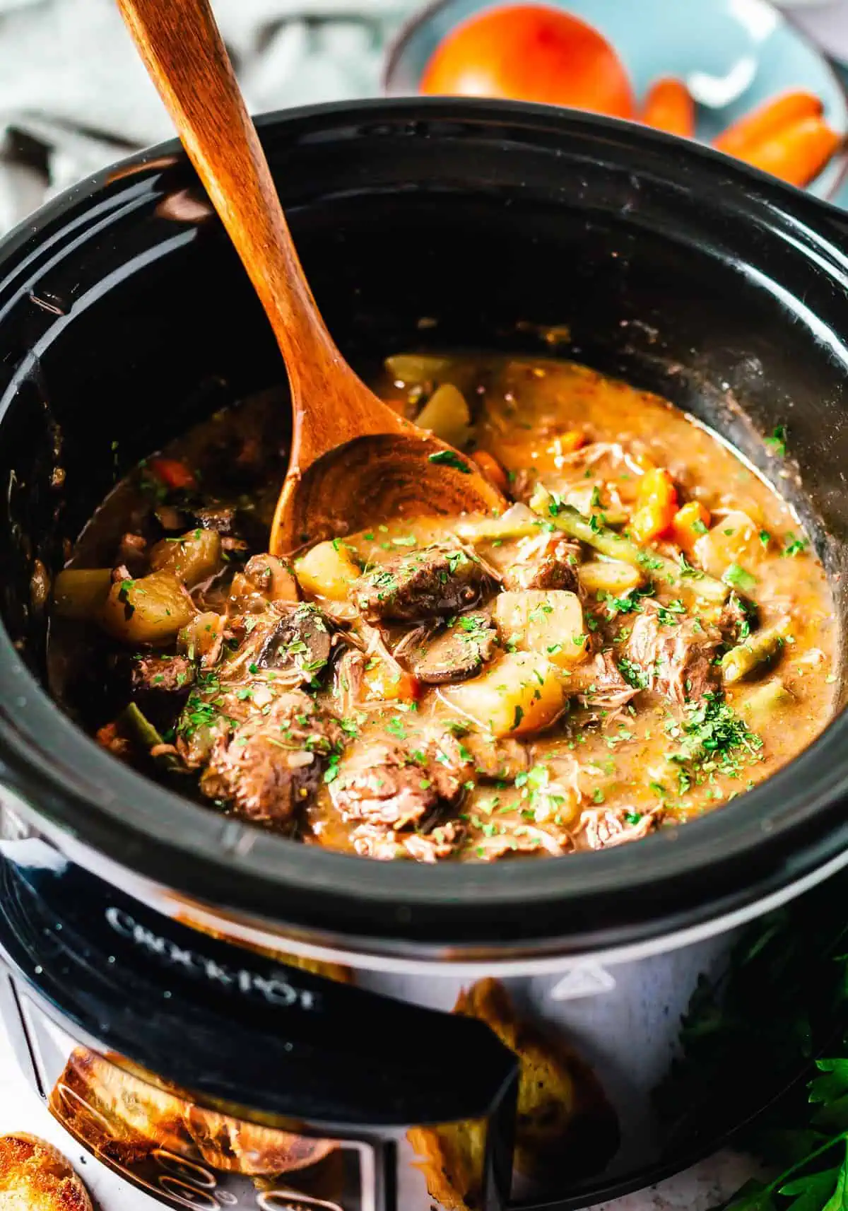 A rich and savory crock pot beef stew in a slow cooker, filled with vegetables and tender beef, with a wooden spoon.