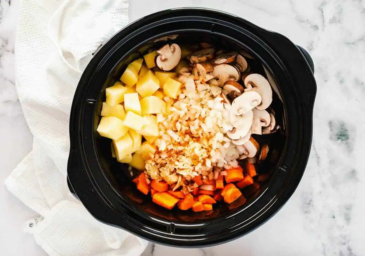 The same slow cooker with vegetables and meat, now sprinkled with cumin, oregano, and paprika.