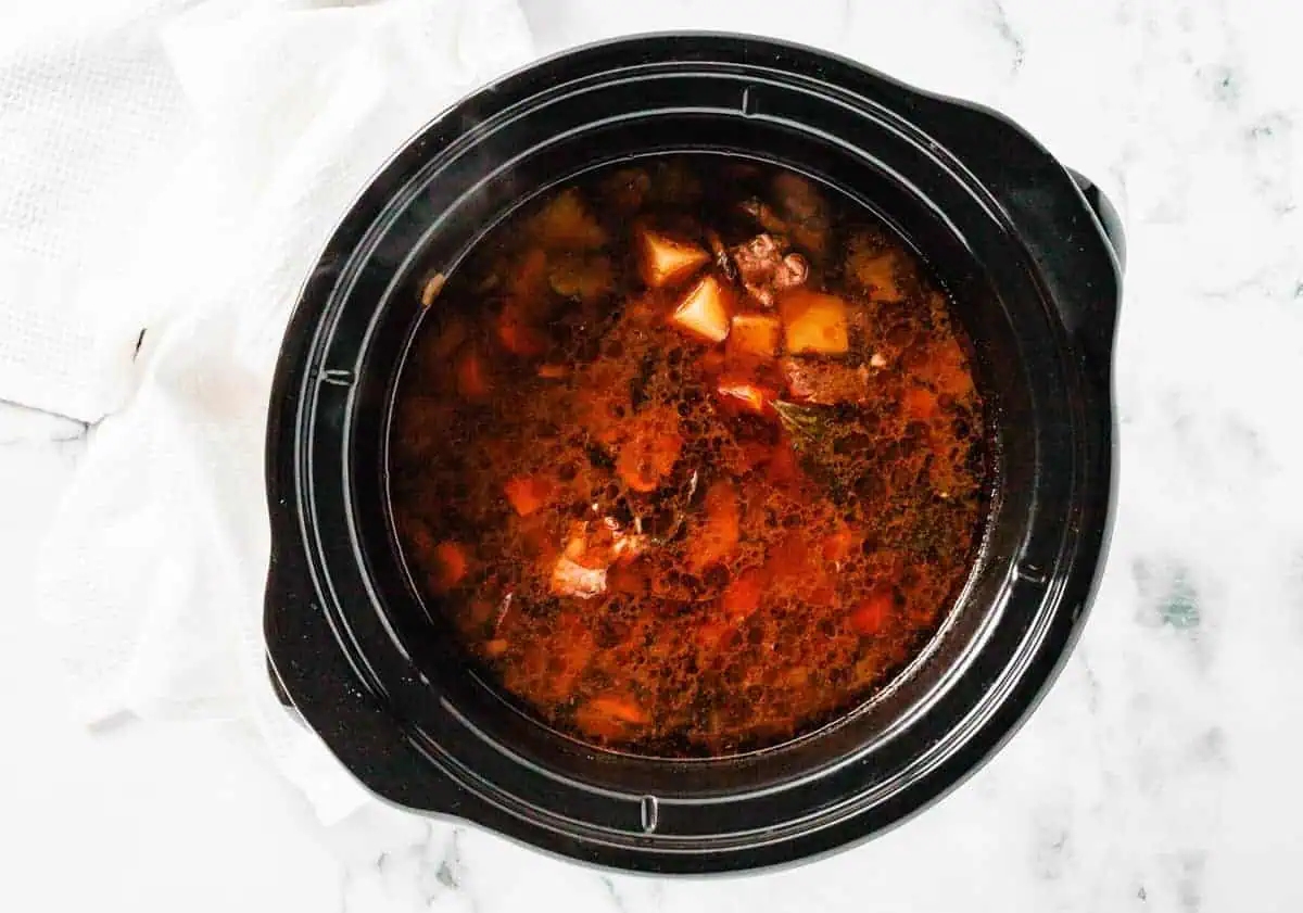 Slow cooker filled with simmering beef stew, showcasing the broth and tender vegetables.