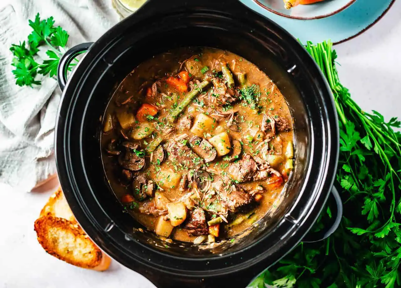 Vibrant slow-cooked beef stew in a crock pot, showcasing tender beef, carrots, green beans, and potatoes, garnished with fresh parsley.