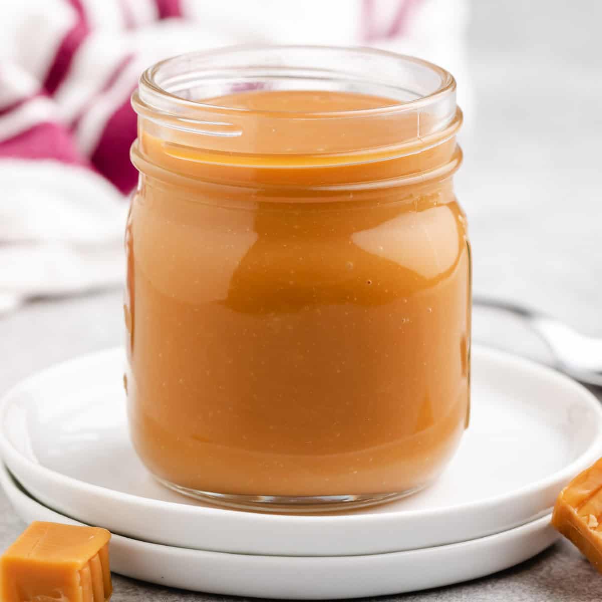 A jar filled with smooth caramel sauce on a white plate.