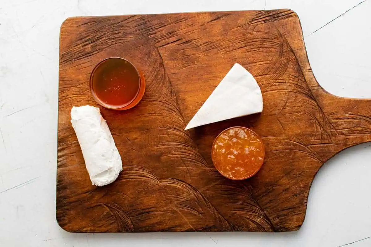 Honey, jam, and cheese on a wooden board.