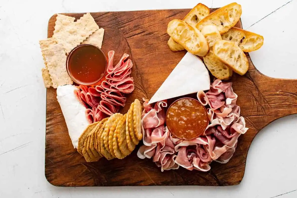 Crackers, honey, jam, cheese and meat on a wooden board.