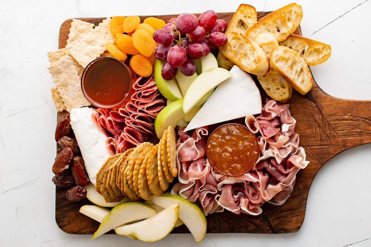 Crackers, fruit, honey, jam, cheese and meat on a wooden board.