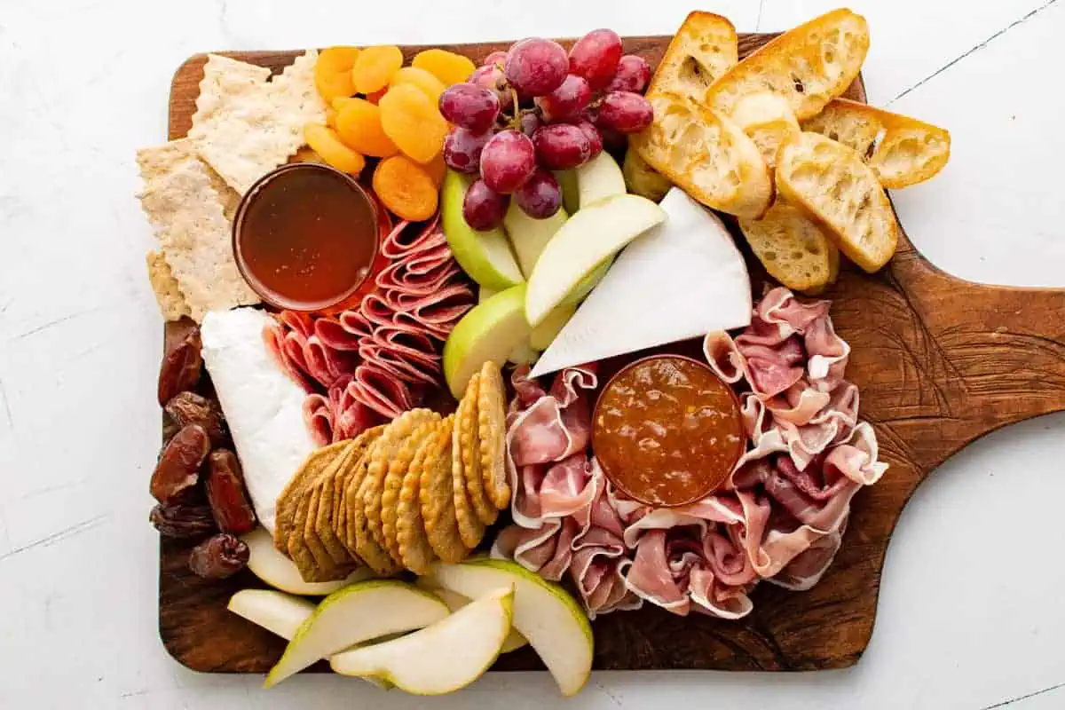 Crackers, fruit, honey, jam, cheese and meat on a wooden board.