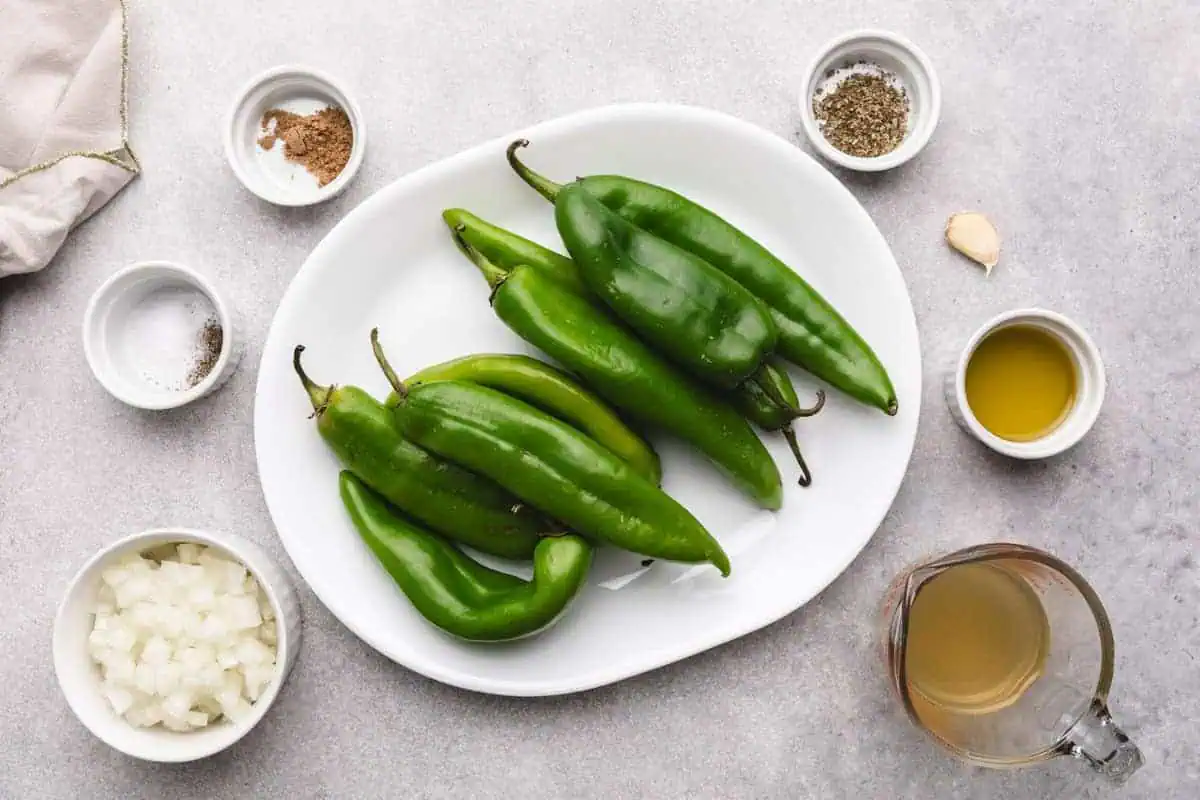 Ingredients for hatch green chile sauce, including fresh hatch chiles, onions, and garlic cloves.