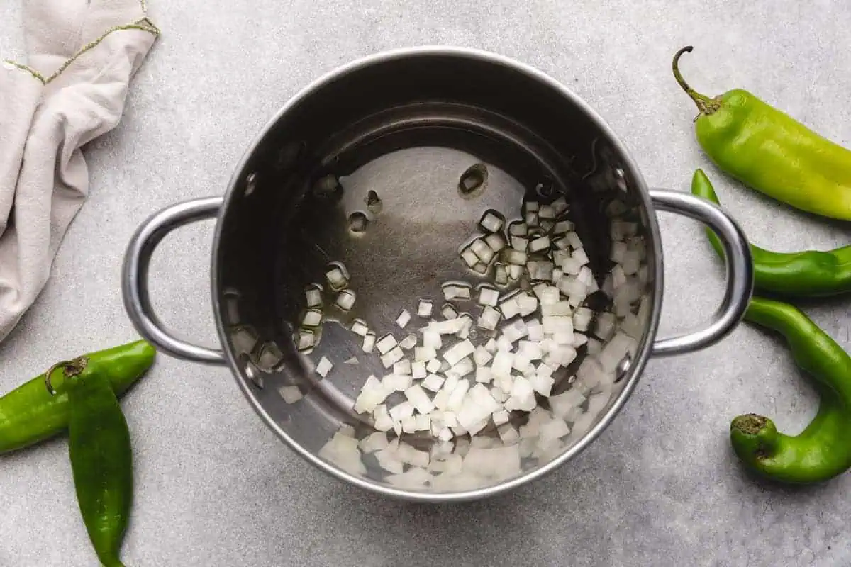 Diced onions sautéing in a saucepan, the base for a rich and flavorful hatch green chile sauce recipe.