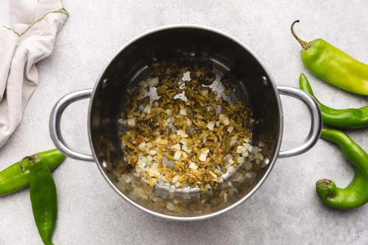 Chopped hatch chiles and onions cooking together in a saucepan.