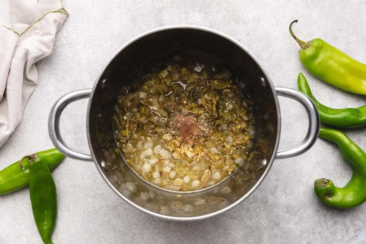 Hatch green chile sauce ingredients, including roasted chiles, onions, garlic, and spices, simmering in a saucepan.