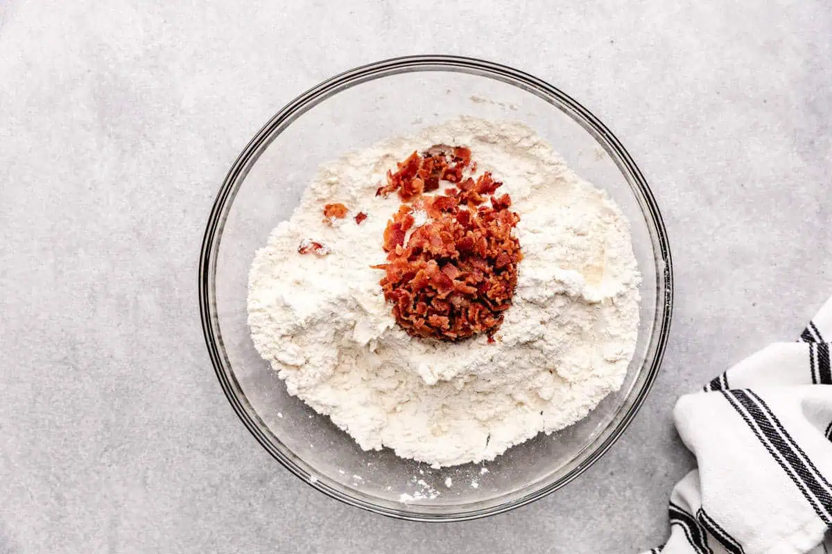 Crumbled bacon poured over a bowl of flour, salt, and baking powder.