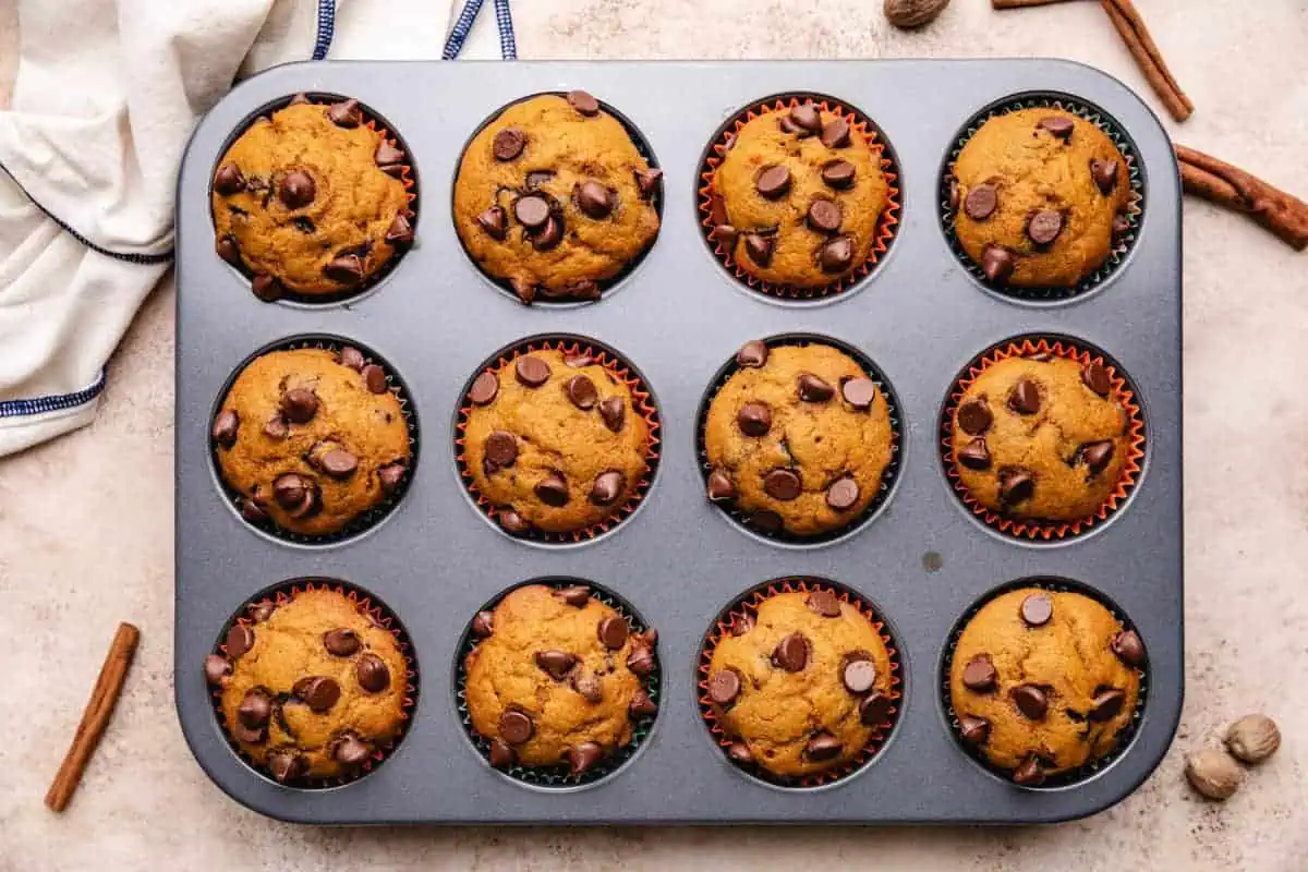 Freshly baked pumpkin chocolate chip muffins in a muffin tin, showcasing the best pumpkin muffin recipe with chocolate chips for fall baking and viral food boards.