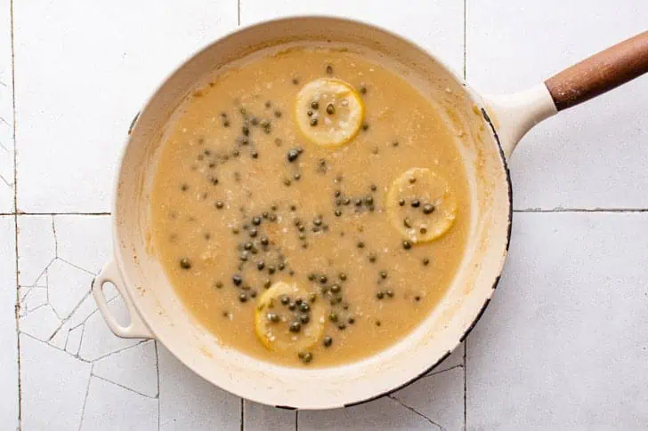 Capers added to a pan of lemon sauce.