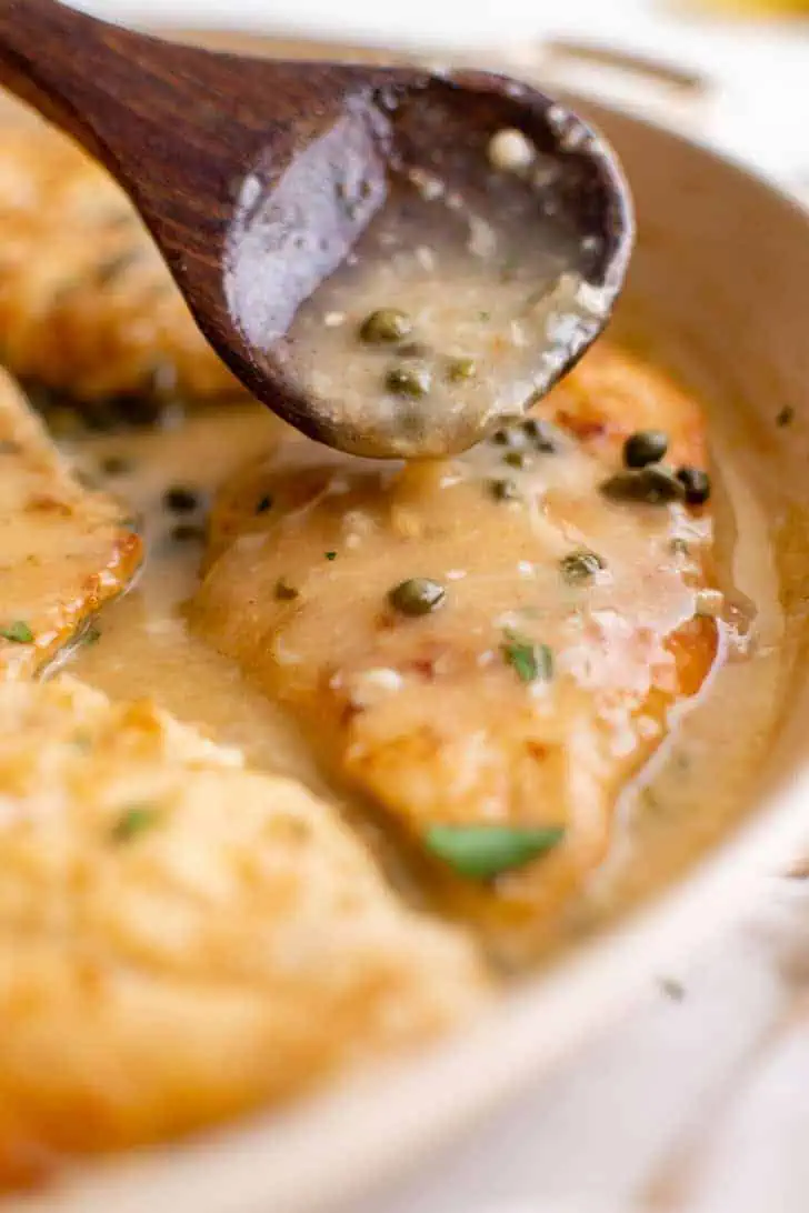 Lemon caper sauce being spoon over a chicken breast.