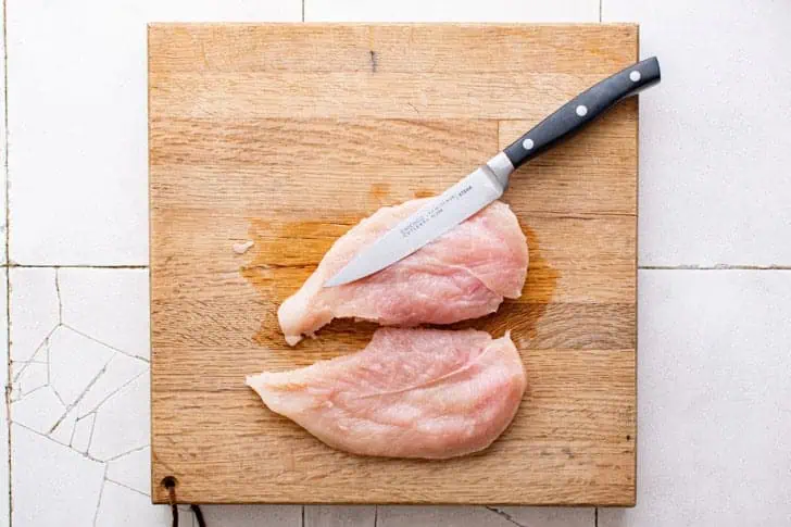 Chicken breast being cut in half lengthwise.