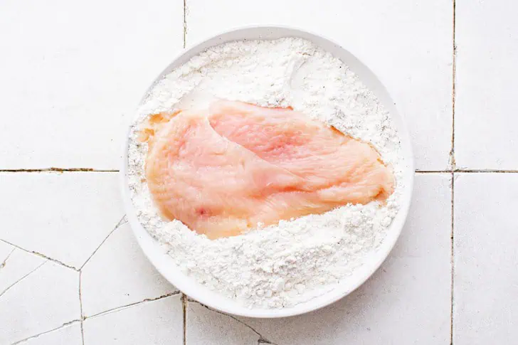 Chicken being dredged in seasoned flour.