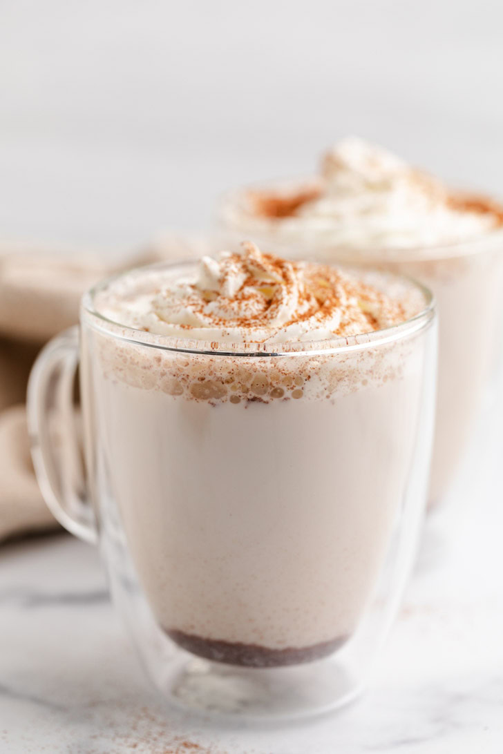 Side view of milk, cinnamon, and maple syrup in a glass mug.