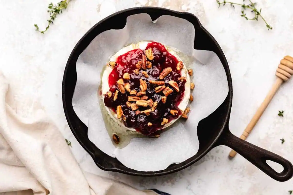 Pecans sprinkled over brie and cranberry sauce.