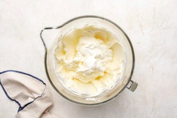 Sour cream added to a bowl of beaten cream cheese.