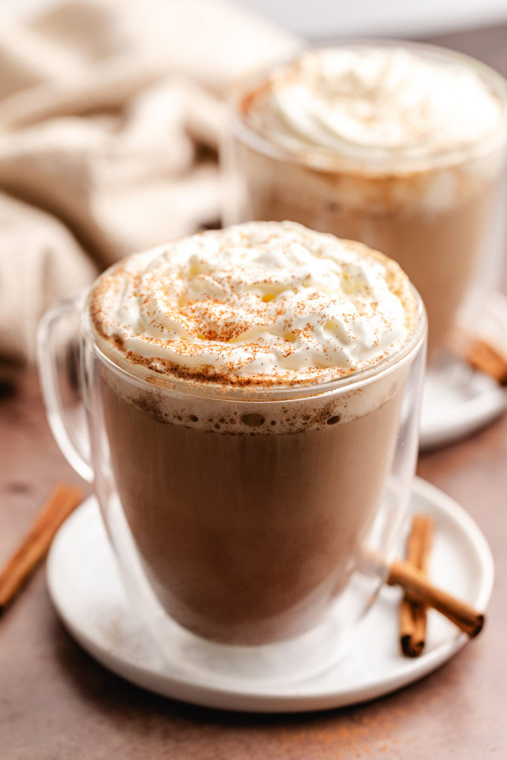 Lattes on plates next to cinnamon sticks.