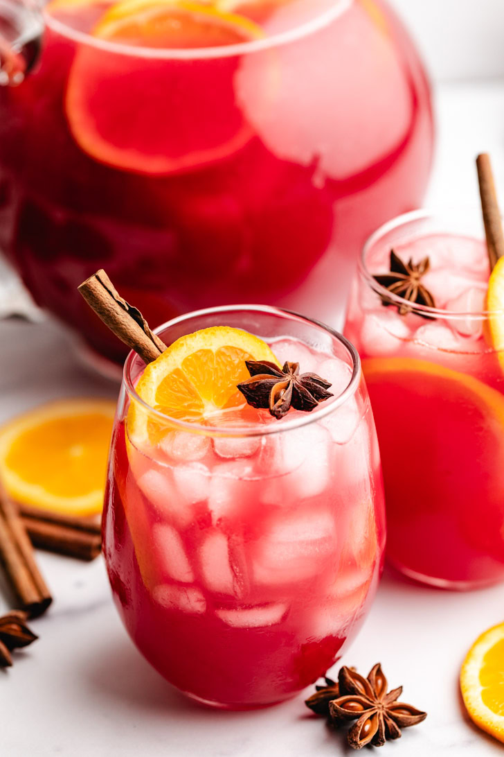 Star anise and orange next to a cranberry drink.