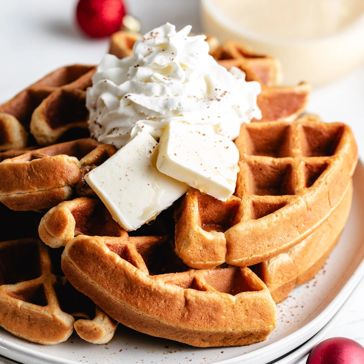 Stack of eggnog waffles topped with whipped cream and butter.