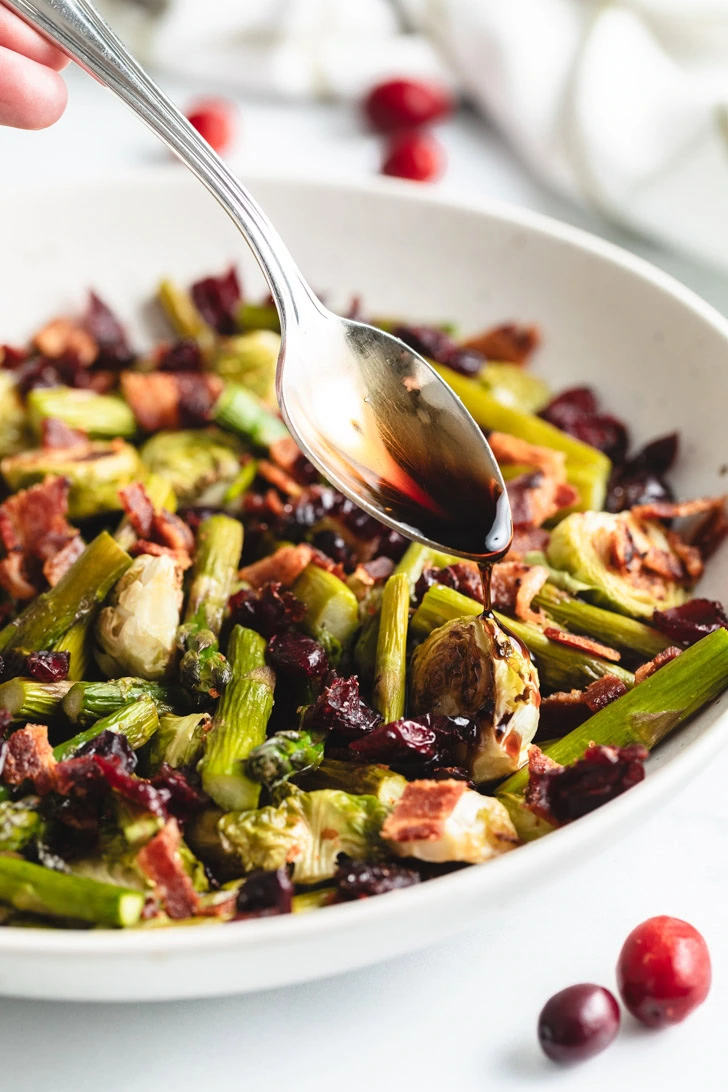 Spoon drizzling balsamic glaze onto a roasted brussels sprout.