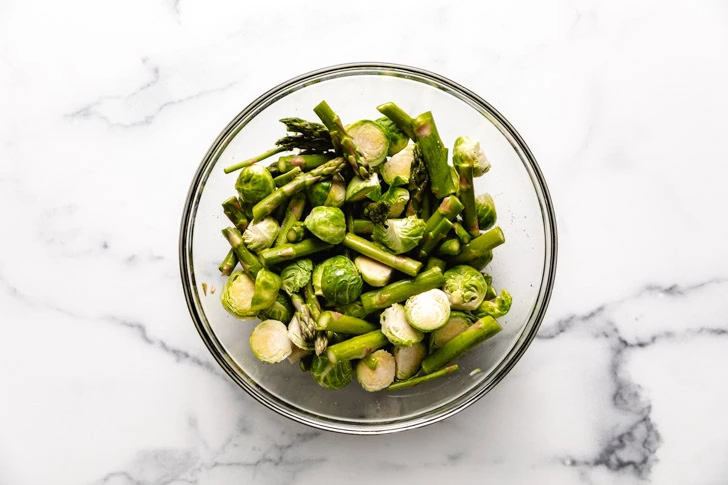 Salted, asparagus, and brussels sprouts in a glass bowl.